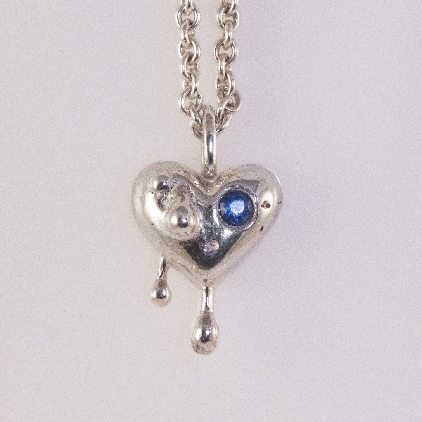 Front view of sand-cast silver heart pendant with small blue zirconia by VerdeRame Jewels