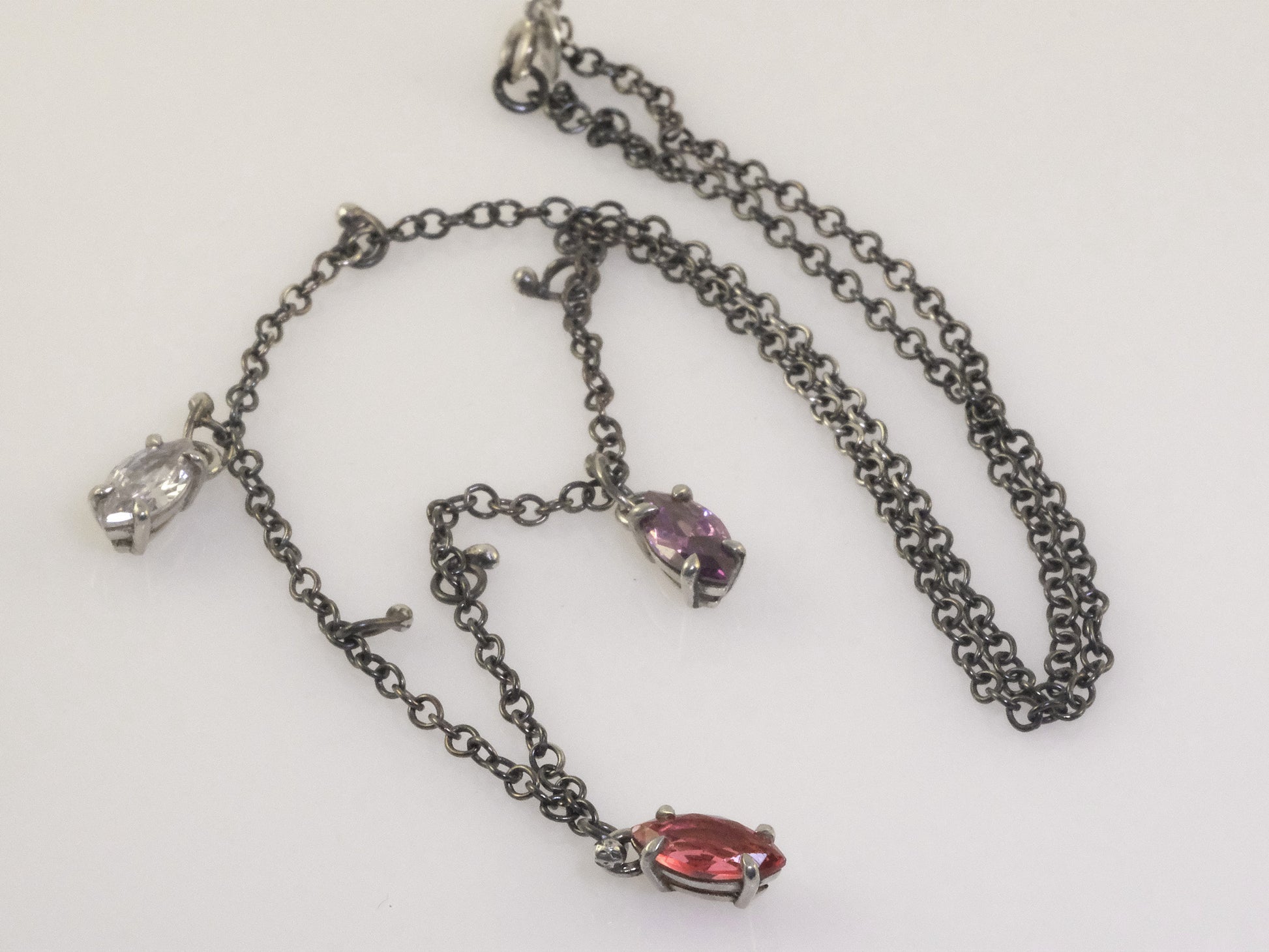 Close-up of marquise crystal pendants in polished silver prong settings on a black oxidised chain.