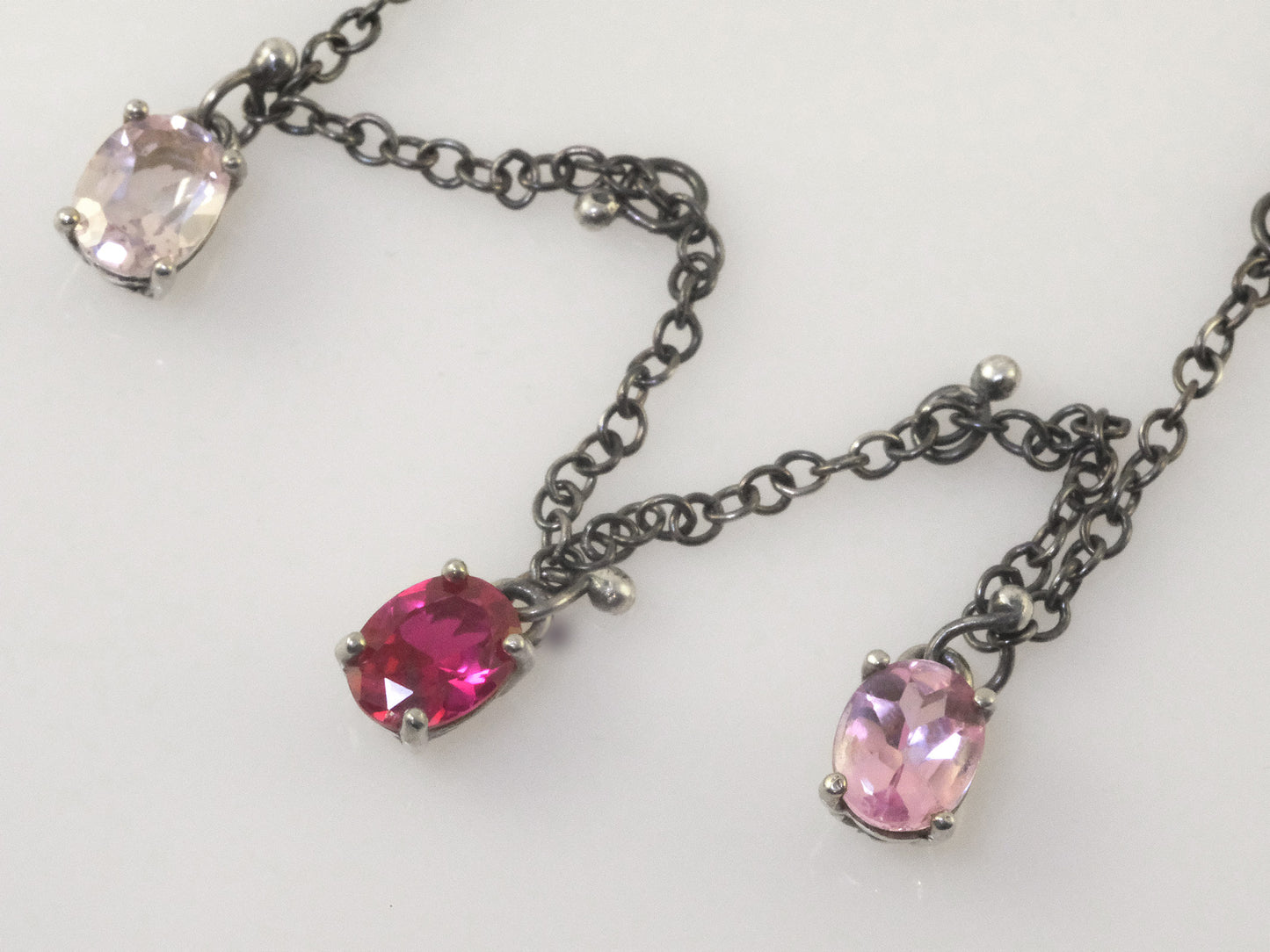 Close-up of three oval crystal pendants in polished silver prongs with small silver ball charms on black oxidised chain.