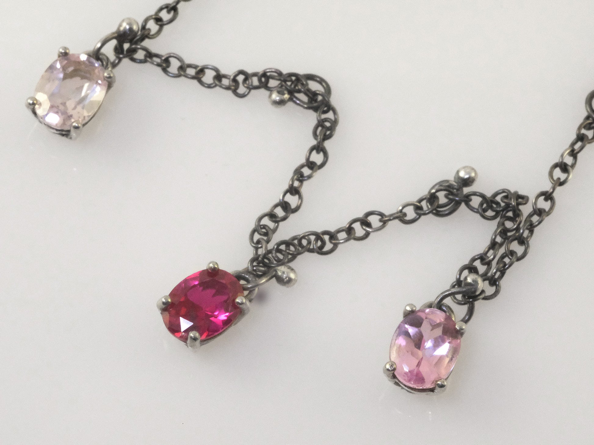 Close-up of three oval crystal pendants in polished silver prongs with small silver ball charms on black oxidised chain.