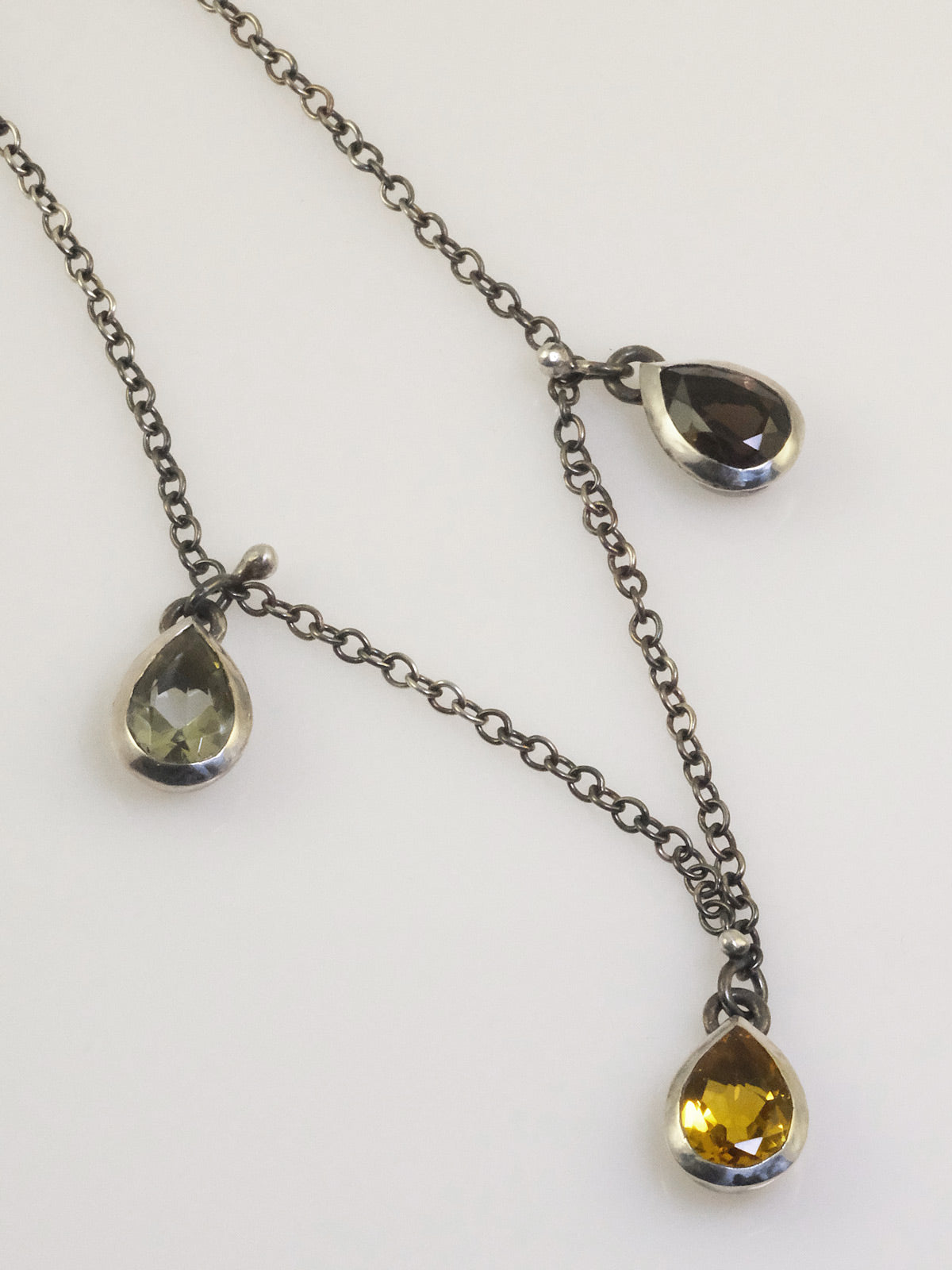 Close-up of teardrop crystal pendants in polished silver bezels on a black oxidised chain.